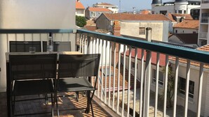 Een balkon met twee stoelen en een tafel, met uitzicht op een stadslandschap met gebouwen en koepelvormige structuren.