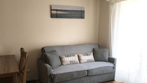 Een grijze bank met twee kussens, een houten tafel en een schilderij aan de muur.