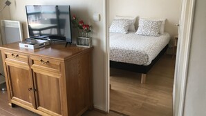 Een slaapkamer met een bed, een televisie op een houten kast en een schilderij aan de muur.