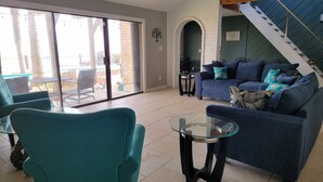 Een woonkamer met teal fauteuils, een glazen salontafel, een blauwe bank met gestreepte kussens en een trap naar een hoger niveau.