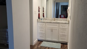 Een moderne badkamer met witte kastjes, een grote spiegel en een houten vloer.
