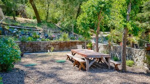 Een houten picknicktafel met banken in een tuin, omgeven door stenen muren en verschillende planten.
