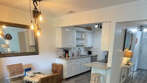 A modern kitchen with white cabinets, a dining area with wicker chairs, and a wooden floor.