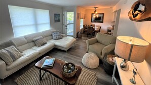 A living room with a sectional sofa, a round coffee table, and a dining area with chairs and a table.