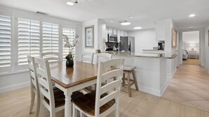 A modern kitchen with white cabinetry, a wooden dining table, and a bar area. - Oceanfront | Ground Floor | Updated Amelia Surf and Racquet Condo (Fernandina Beach)