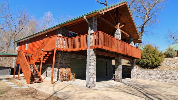 A two-story log cabin with a wooden balcony, stone foundation, and a garage. - Grand Lake Cabin Retreat - Lake, Dock, & Woods (Vinita)