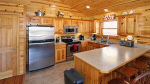 A spacious kitchen with wooden cabinets, stainless steel appliances, and a large island. - Grand Lake Cabin Retreat - Lake, Dock, & Woods (Vinita)
