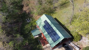 A house with a green roof and solar panels, surrounded by trees and a small patio area. - Grand Lake Cabin Retreat - Lake, Dock, & Woods (Vinita)
