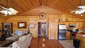 A log cabin interior with a wooden ceiling, a dining area, a kitchen with modern appliances, and a cozy living room with a sofa and fireplace. - Grand Lake Cabin Retreat - Lake, Dock, & Woods (Vinita)