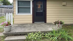 A single-story house with a dark front door, a garage door, and a small porch with steps leading to the door. - Enjoy a Lake Huron view less than a minute walk to the beautiful sandy beach. (Au Gres)