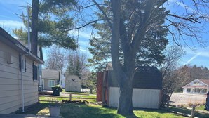A residential yard with a house, a large tree, a shed, and a small garden area. - Enjoy a Lake Huron view less than a minute walk to the beautiful sandy beach. (Au Gres)