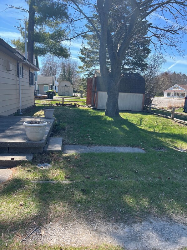 A residential yard with a house, a large tree, a shed, and a small garden area. - Enjoy a Lake Huron view less than a minute walk to the beautiful sandy beach. (Au Gres)