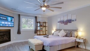 Un dormitorio con cama, ventilador de techo, chimenea, televisor y estantería.