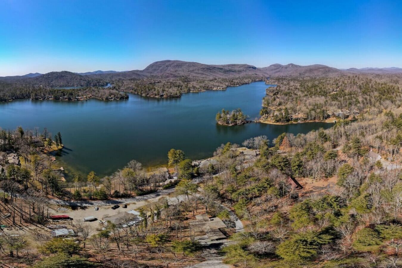 Ein See, umgeben von bewaldeten Hügeln und einer kleinen Siedlung mit erkennbaren Gebäuden und Wegen.