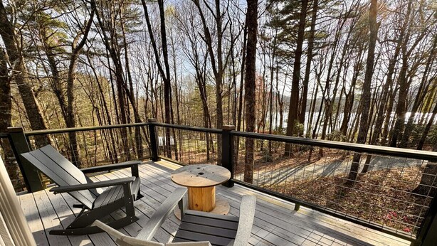 Una terraza de madera con dos sillas Adirondack y una mesa redonda de madera.