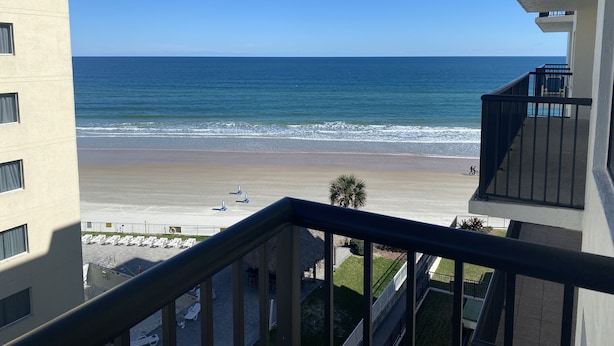 A beachfront view from a balcony with a clear sky, a sandy beach, and a calm sea.