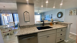 A kitchen with granite countertops, a stainless steel sink, and a dishwasher. There is a ceiling fan and recessed lighting.