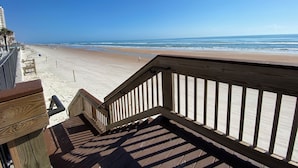 A wooden deck leading to a beach with a clear view of the ocean and a few people in the distance.