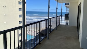 A balcony with a view of the ocean, a pool, and a building with multiple windows.