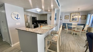 A kitchen with granite countertops, stainless steel appliances, and a dining area with a white table and chairs.
