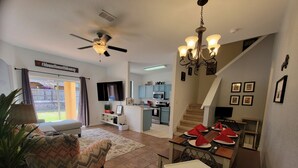 A spacious living room with a sofa, a dining table set for four, a kitchen in the background, and a staircase leading to an upper level. - Fun Family Themed Resort home close to Disney. Regal Palms Resort  (Davenport)