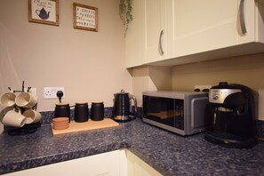 A kitchen with a microwave, coffee maker, and a cutting board with cups.