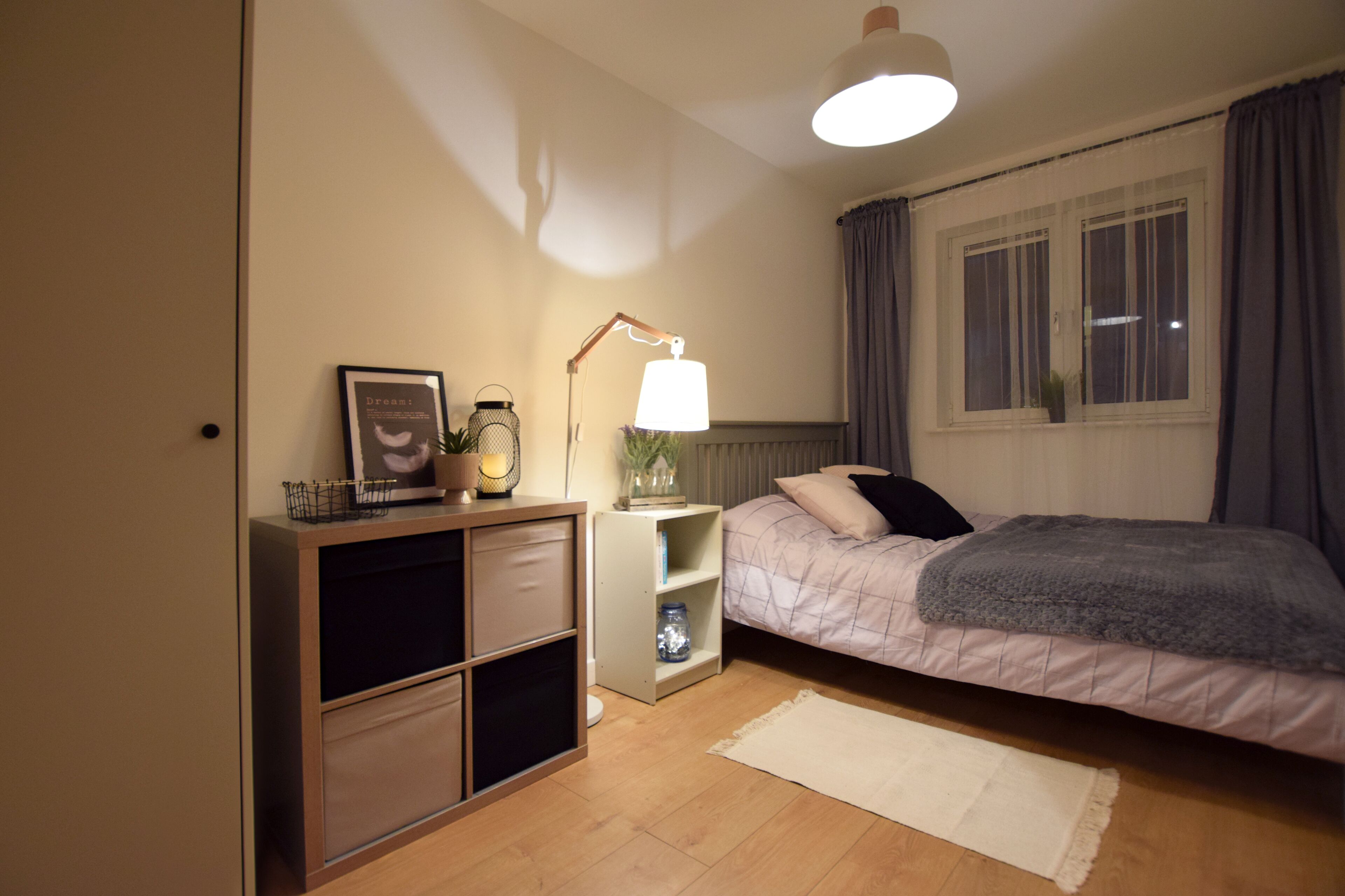 A bedroom with a bed, bedside table, lamp, and a window with curtains.