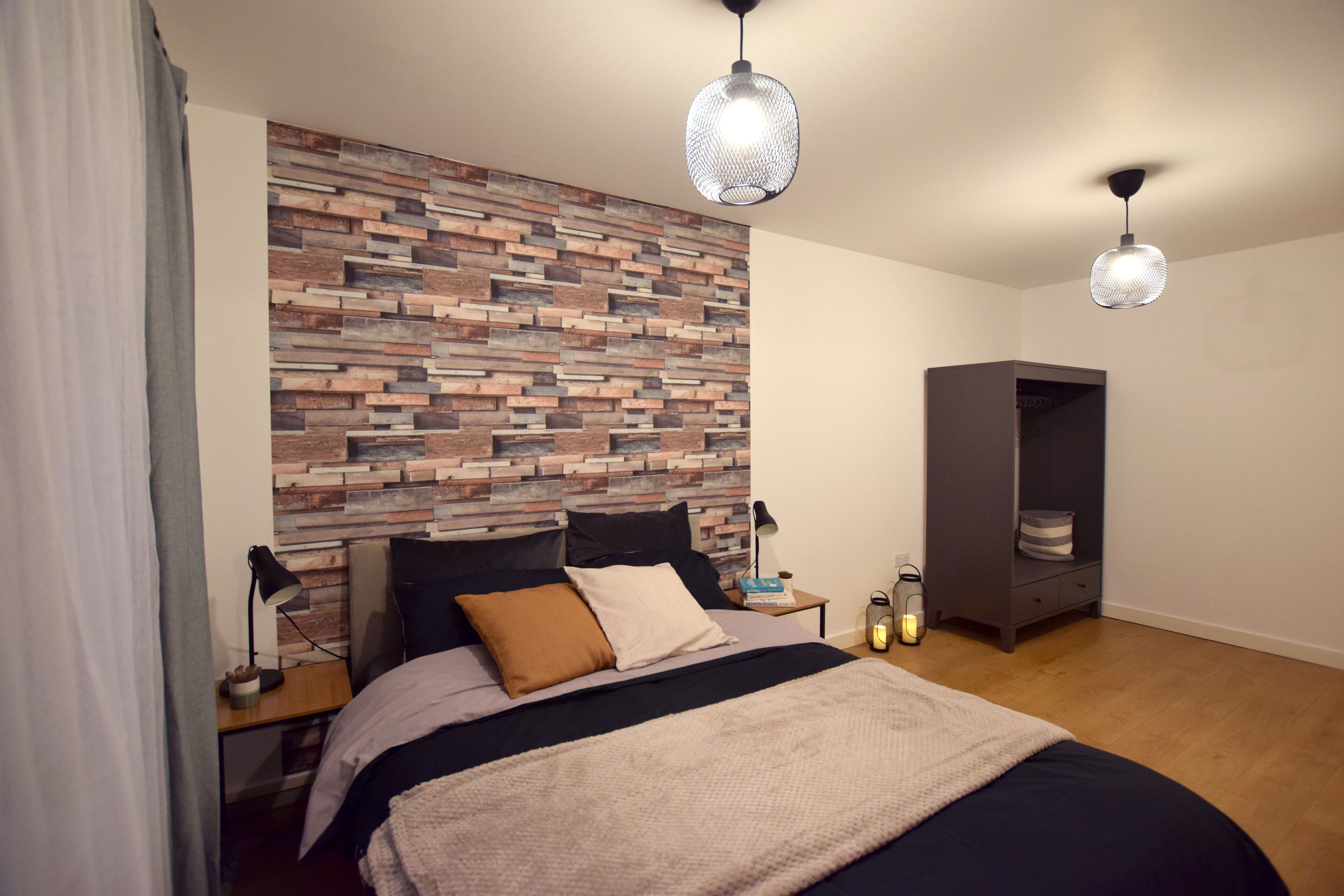 A bedroom with a bed, a nightstand, a lamp, a bookshelf, and a wall with a wooden plank design.