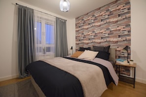A bedroom with a bed, a nightstand, a lamp, and a wall with a wooden pattern.