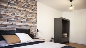 Ein Schlafzimmer mit Bett, Nachttisch, Lampe, Kleiderschrank und einer Wand mit Holzpaneelen.