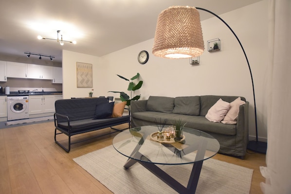 A modern living room with a glass coffee table, a sofa, and a hanging light fixture.