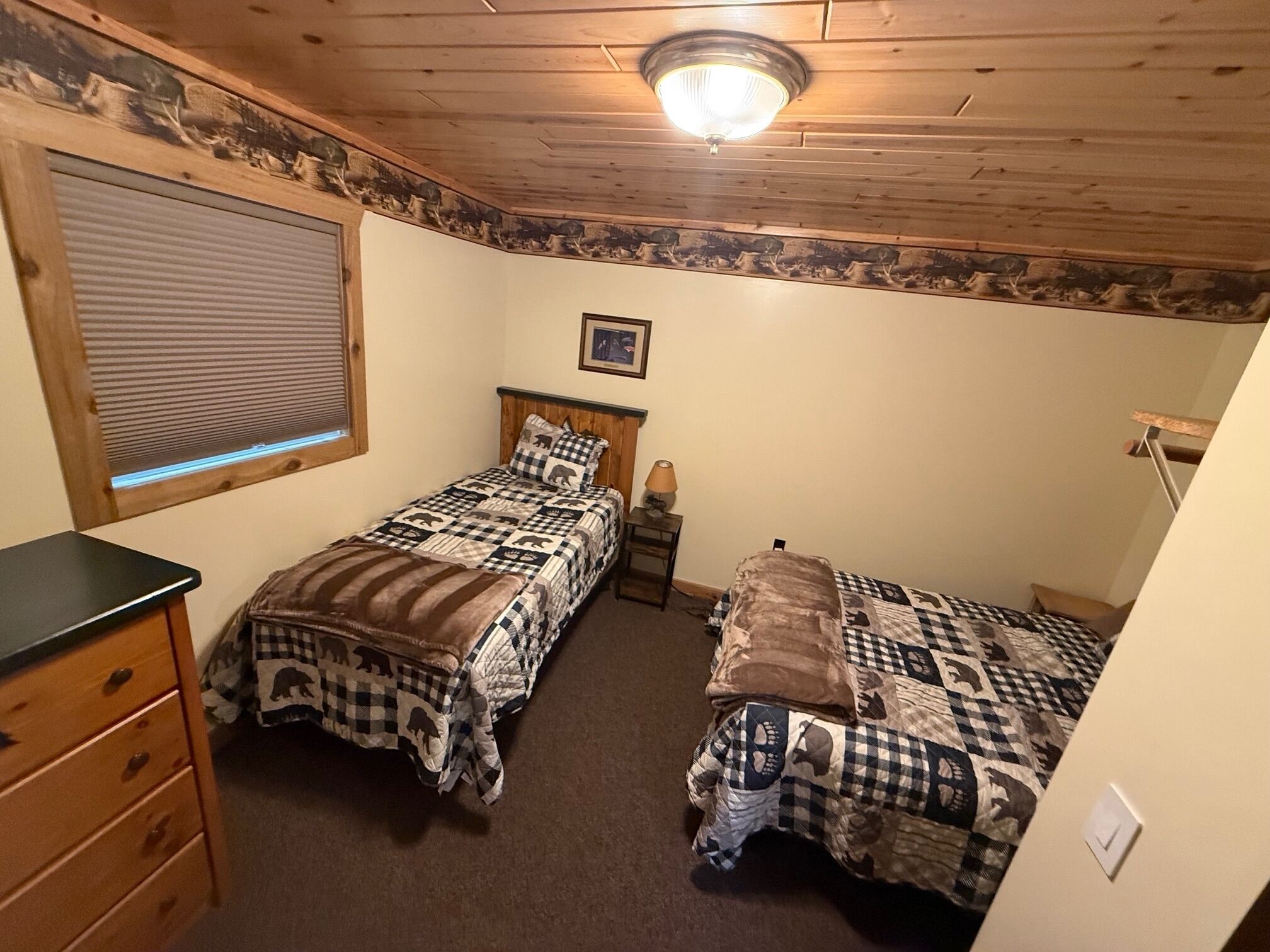 A bedroom with two beds, a dresser, a window with blinds, a ceiling light, and a framed picture on the wall.