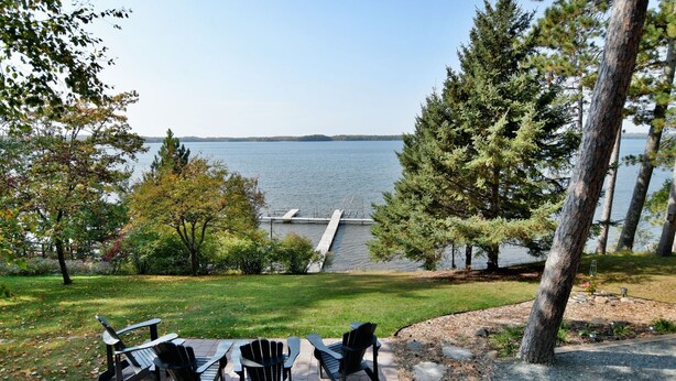 A lakeside patio with Adirondack chairs and a dock extending into the water. - Top Boating, fishing, swimming-summer AND winter destination in Wisconsin! (Hayward)