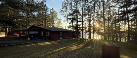 A cabin with a garage, surrounded by tall trees and a clear sky.