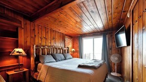 A wooden cabin bedroom with a bed, a lamp, a TV, and a fan. - Top Boating, fishing, swimming-summer AND winter destination in Wisconsin! (Hayward)