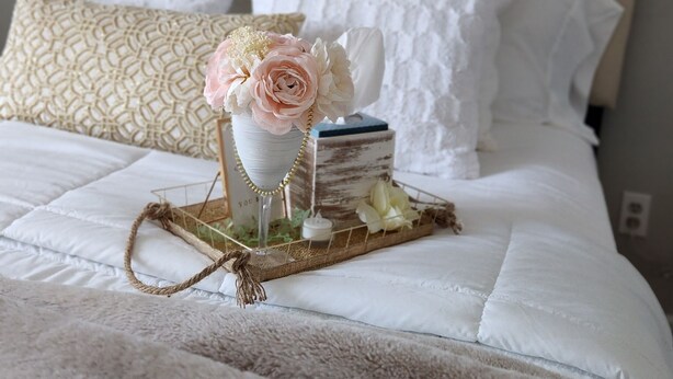 A neatly made bed with a decorative centerpiece, a wall with a sign, and a textured wall.