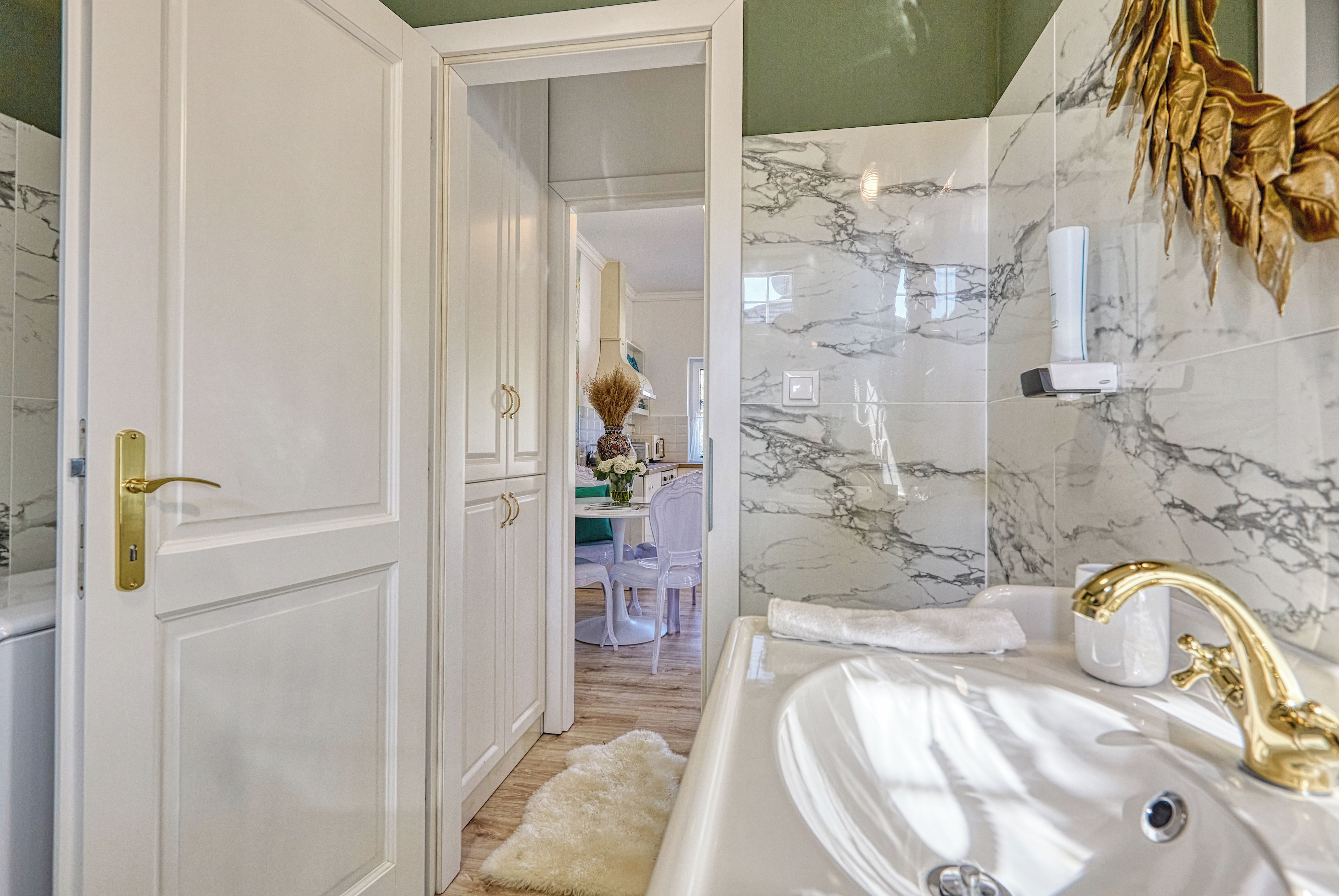 A bathroom with a white sink, gold faucet, and marble walls.