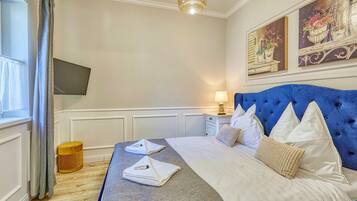 Een hotelkamer met een bed, een nachtkastje met een lamp, een klein krukje en een aan de muur bevestigde televisie.