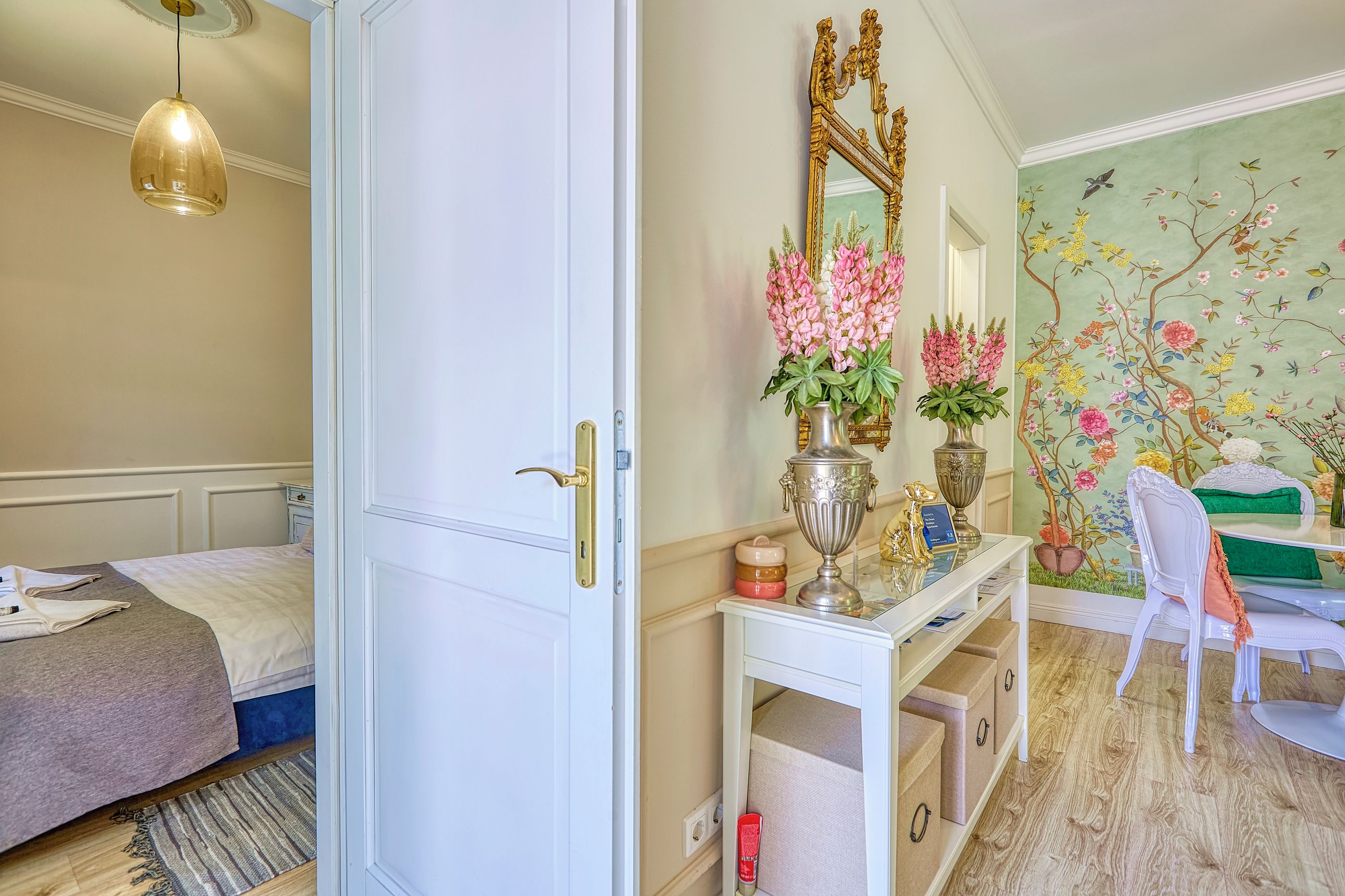 Un dormitorio con cama, armario blanco, tocador con espejo y un mural floral en la pared.