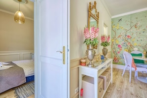 A bedroom with a bed, a white wardrobe, a vanity with a mirror, and a floral wall mural.
