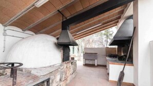 An outdoor kitchen area with a stone oven, a grill, and a hanging pot rack.