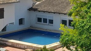 A residential property with a swimming pool, a tiled roof, and a white exterior wall.