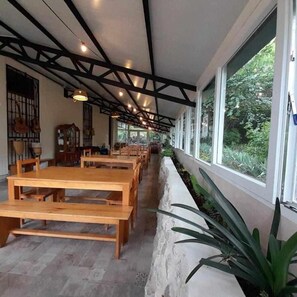 A long dining area with wooden tables and benches, a stone wall with plants, and large windows offering a view of greenery. - Cozy rural accommodation ideal for groups (Agres, Alicante)