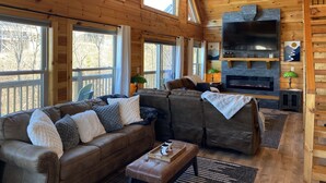 Ein gemütliches Blockhaus-Interieur mit einer großen Holzbalkendecke, Kamin, Sofa und Fernseher.