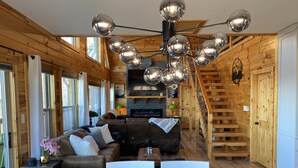 Ein gemütliches Holzinnere mit einem modernen Kronleuchter, einem Kamin und einer Treppe.