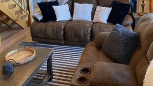 Ein gemütliches Wohnzimmer mit einem braunen Ledersofa, einem Holzesstisch und einer Küche im Hintergrund.