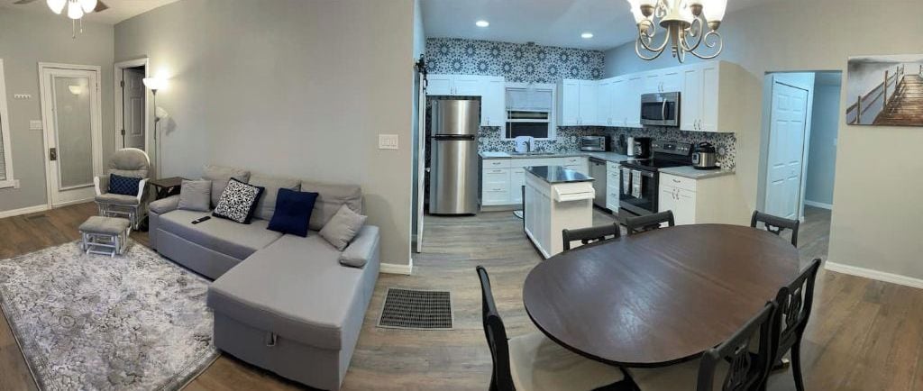 A modern living room with a grey sofa, a dining table, and a kitchen in the background.