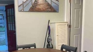 A round wooden table with six chairs, a chandelier, and a painting of a pier on the wall. - All New Deland Den 4BR, pool, blocks fr Stetson & Downtown (DeLand)