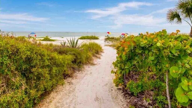 A sandy path leading to a beach with palm trees and beach umbrellas. - Brand New to the rental market ! (Sanibel)