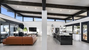 A spacious living area with a large sofa, a flat-screen TV, and a dining area with a kitchen in the background.